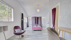 Habitació d'hotel moderna amb un llit, una cadira morada, una taula de fusta i una finestra gran.