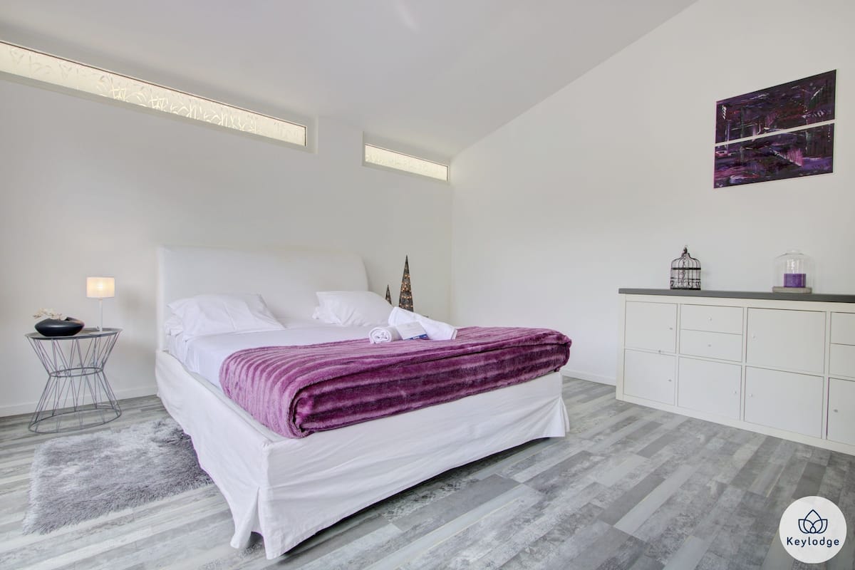 Un dormitorio moderno con una cama grande, una mesita auxiliar pequeña, una jaula decorativa y un mueble con cajones.
