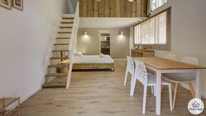 Un dormitori d'estil loft amb una escala de fusta, un llit, un escriptori i una zona de menjador.