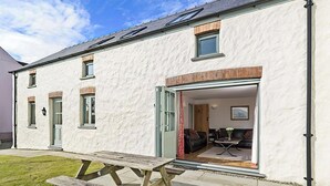 A white building with a patio area featuring a wooden table and benches. - 2 bedroom accommodation in Dwrbach, near Fishguard (Dwrbach, near Fishguard)