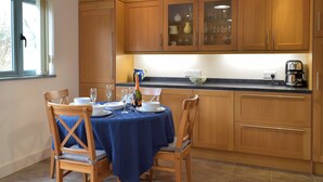 A kitchen with wooden cabinets, a dining table set for four, and a coffee maker on the counter. - 2 bedroom accommodation in Dwrbach, near Fishguard (Dwrbach, near Fishguard)