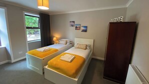 A hotel room with two single beds, a wardrobe, a window with curtains, a lamp, and a wall with a 'LOVE' sign. - 4 bedroom accommodation in Newton Stewart (Newton Stewart)
