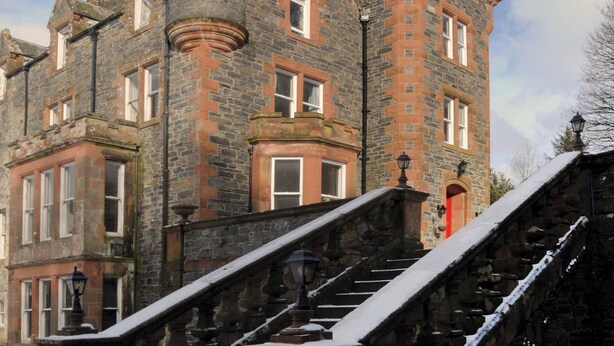 A historic stone building with multiple windows, a turret, and a staircase leading to the entrance. - 4 bedroom accommodation in Newton Stewart (Newton Stewart)