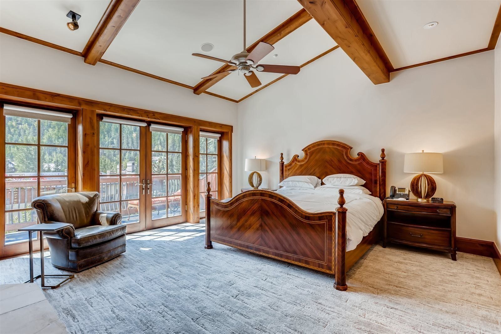 A spacious bedroom with a large bed, a wooden headboard, a nightstand with a lamp, and a chair.