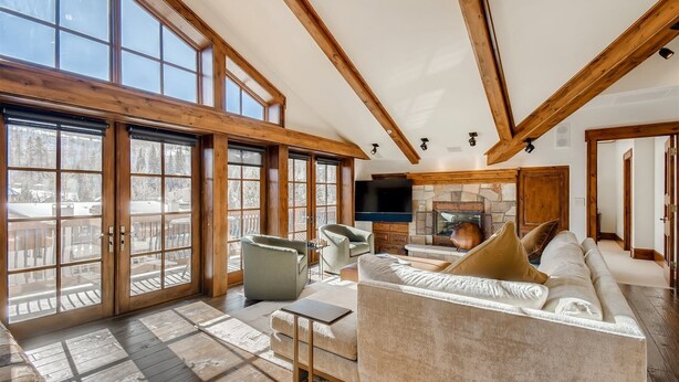 A spacious living room with a large fireplace, wooden beams, and a balcony with glass doors. - 1-#42 4BD One Willow Bridge Road (Vail)