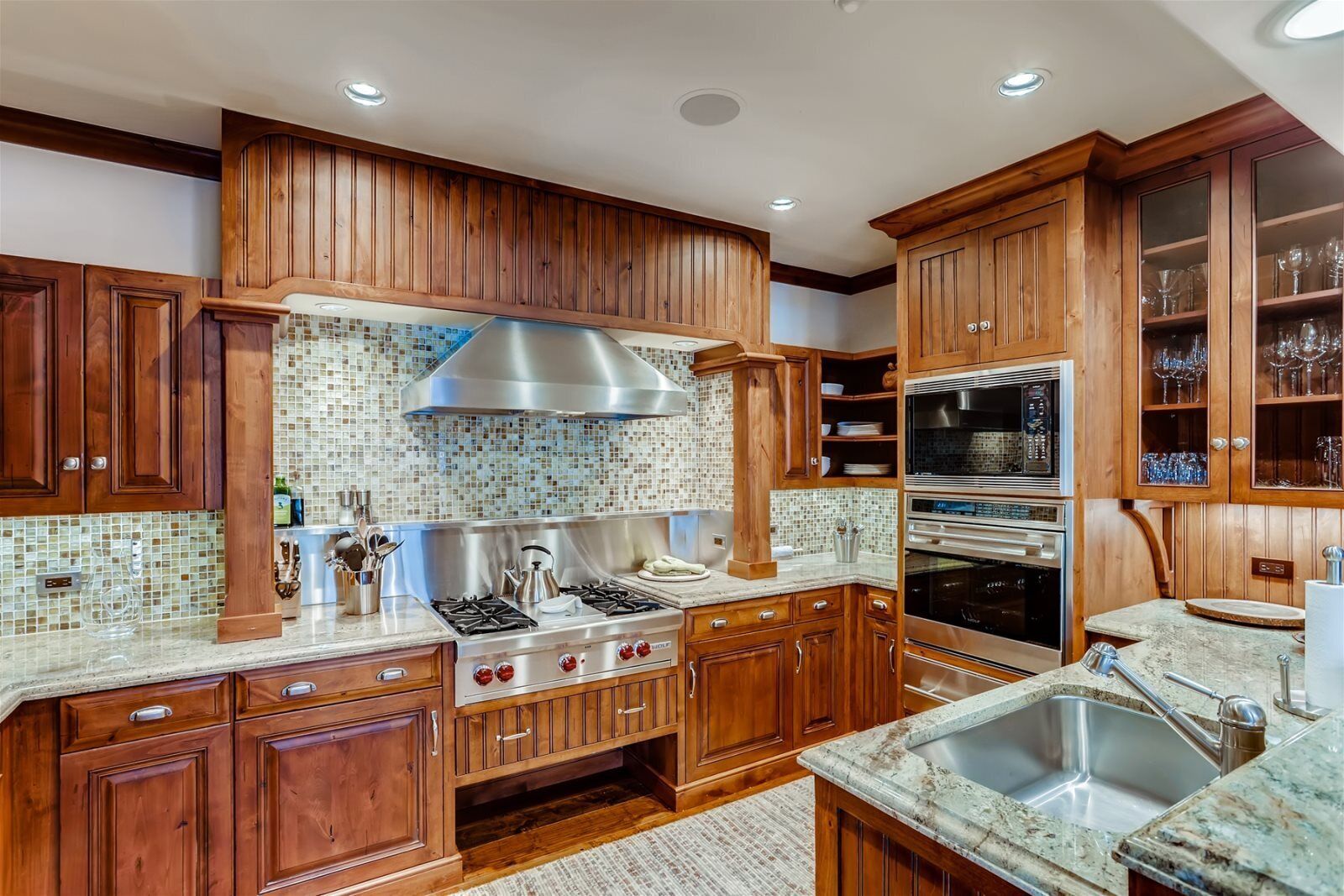 Una cocina con armarios de madera, estufa a gas, microondas y horno empotrado.