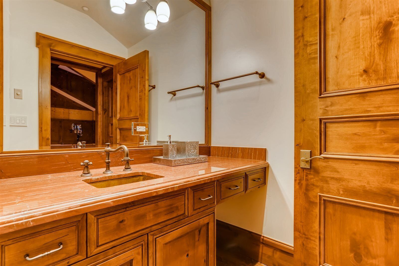 Un baño de madera con un espejo grande, un lavabo con grifo antiguo y un perchero para toallas.