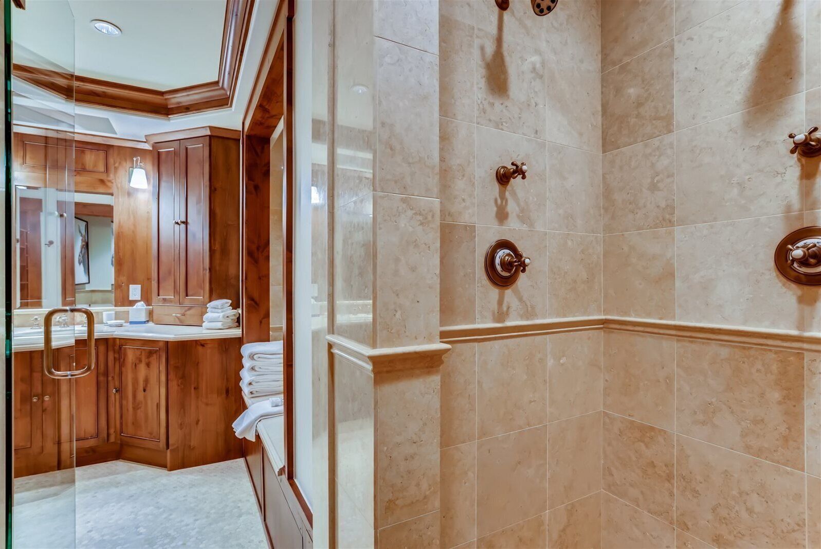 Ein Badezimmer mit Waschtisch aus Holz, einem großen Spiegel und einer Dusche mit beigen Fliesen.
