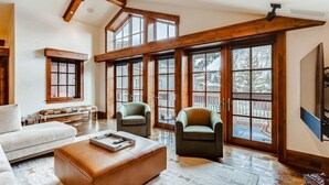 A spacious living room with a high ceiling, wooden beams, large windows, and a cozy seating area. - 1-#42 4BD One Willow Bridge Road (Vail)