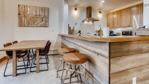 A modern kitchen with a wooden island, bar stools, and a dining table with chairs. - 1-brookside 307 (Avon)
