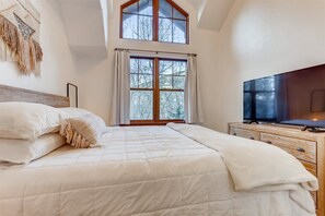 A bedroom with a large bed, a TV, and a window with curtains. - 1-brookside 307 (Avon)