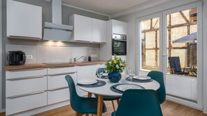 A modern kitchen with white cabinets, a built-in oven, and a dining area with a round table and teal chairs.