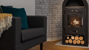 A modern living room with a black sofa, teal cushions, and a wood-burning stove.