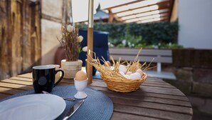 A wooden table with a black mug, white egg cups, and a wicker basket containing eggs.