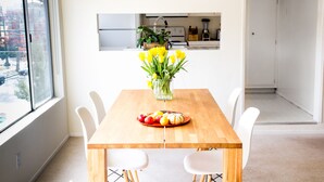 En matplats med ett träbord, vita stolar, en vas med gula blommor och en fruktfat.