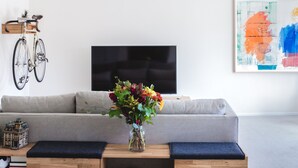 Ett modernt vardagsrum med en grå soffa, ett träbord med en vas med blommor, en cykel som hänger på väggen och en platt-TV.