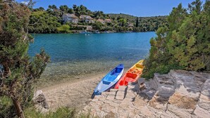 A rocky shoreline with kayaks and a lake with buildings in the background. - Luxury Beachfront Villa Blue Star Brac with Pool (Milna)