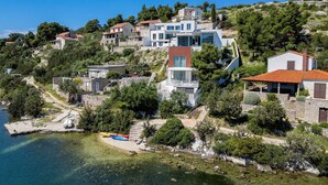 A coastal village with stone buildings, a clear blue sea, and a sandy beach with kayaks. - Luxury Beachfront Villa Blue Star Brac with Pool (Milna)