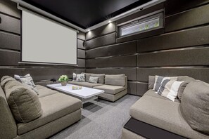 A modern home theater with sectional sofas, a white coffee table, and a large screen.