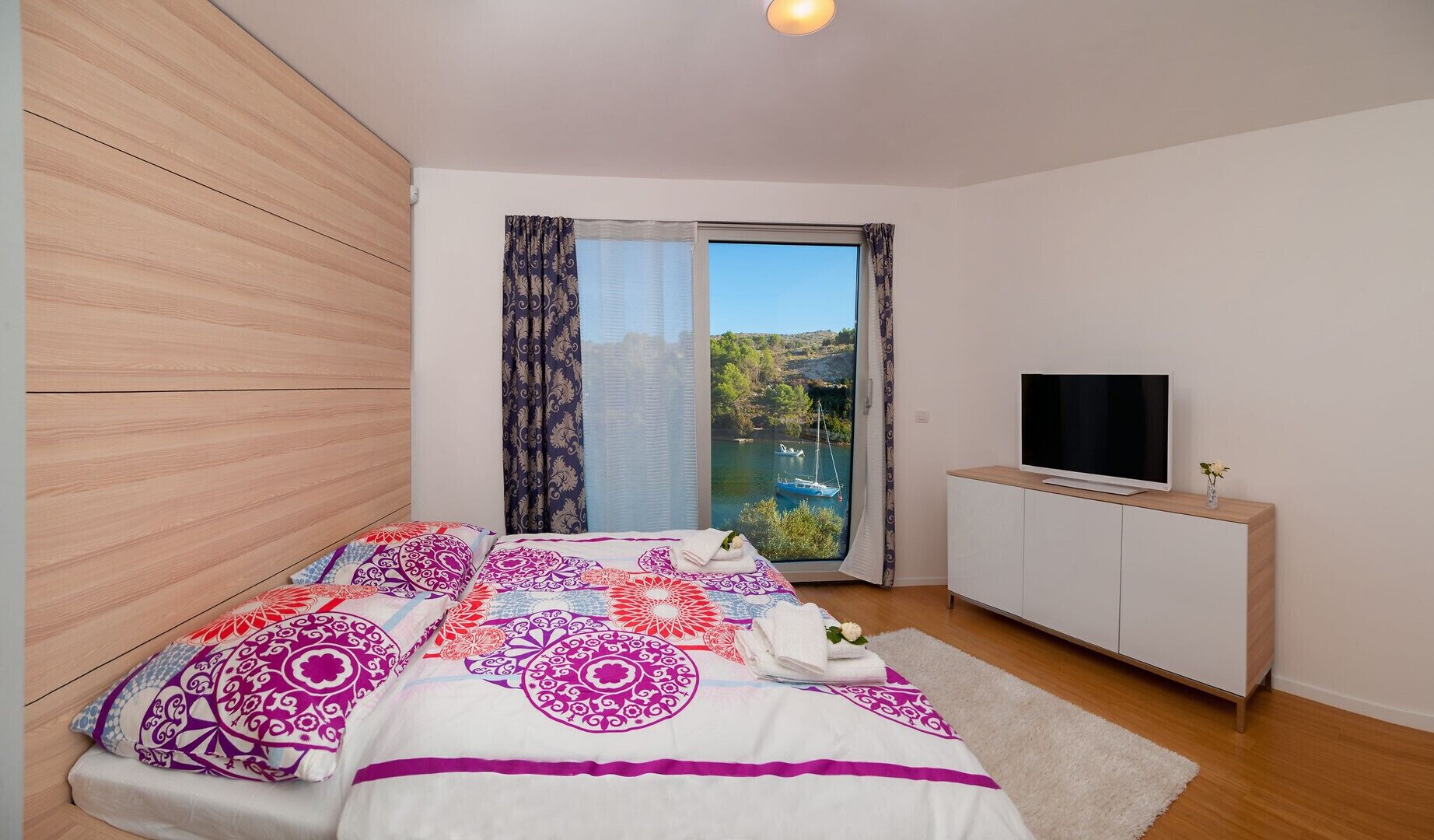 Een slaapkamer met een bed, een televisie en uitzicht op een waterpartij.