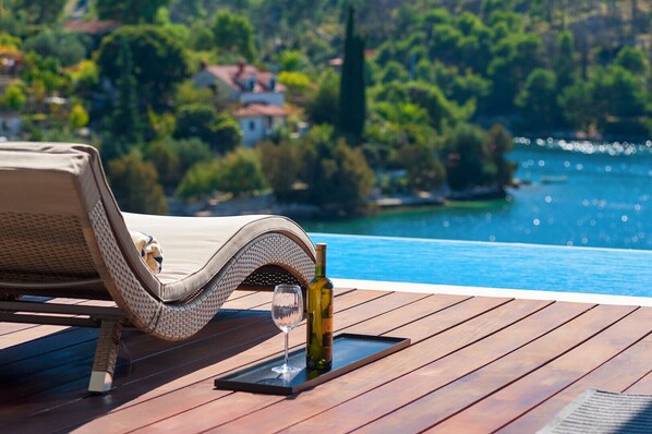 A lounge chair on a wooden deck overlooking a body of water with a bottle and glass.