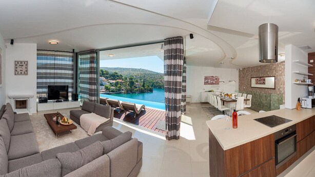 A modern living room with a sofa, TV, and fireplace, leading to a balcony with a pool view. - Luxury Beachfront Villa Blue Star Brac with Pool (Milna)