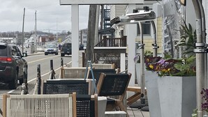 Ein Restaurant am Meer mit Außenbereich, einem Schild mit der Aufschrift 'STONES THROW' und Blick auf die Straße.