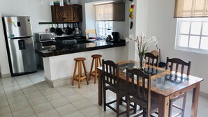 A modern kitchen with a stainless steel refrigerator, a microwave, and a stove. There is a dining table with wooden chairs and two stools. - Apartment half a block from the sea (San Miguel de Cozumel)