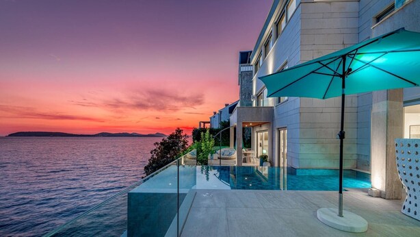 A modern building with a glass infinity pool overlooking the sea, a patio area with outdoor seating, and a large umbrella. - Luxury Seafront Villa Dubrovnik Lux Life with Pool (Dubrovnik)