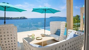 An outdoor seating area with two turquoise umbrellas, a pool, and a view of the sea. - Luxury Seafront Villa Dubrovnik Lux Life with Pool (Dubrovnik)