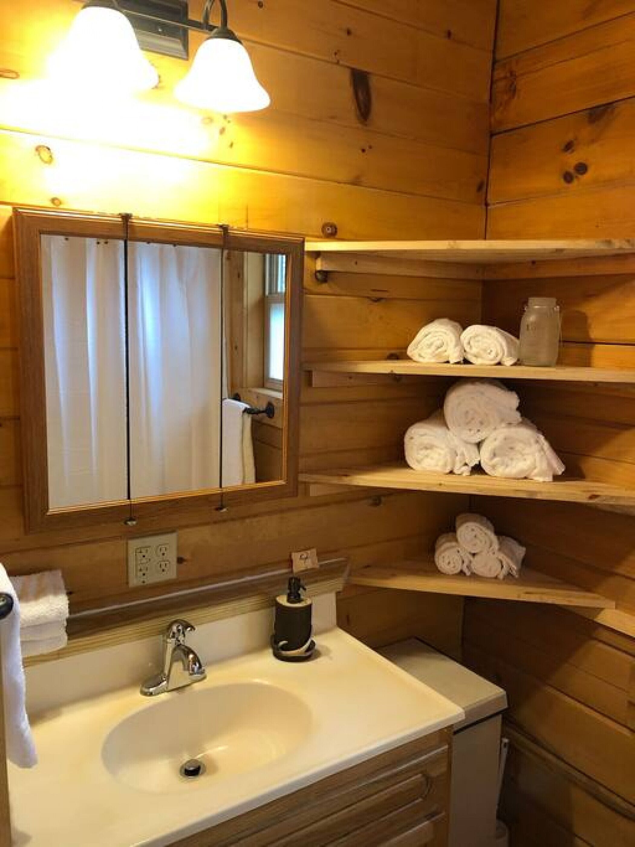 A wooden cabin bathroom with a sink, mirror, and shelves holding rolled towels.