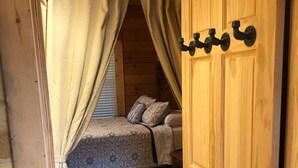 Ein Schlafzimmer einer Holzhütte mit Bett, Vorhängen und einer Tür.
