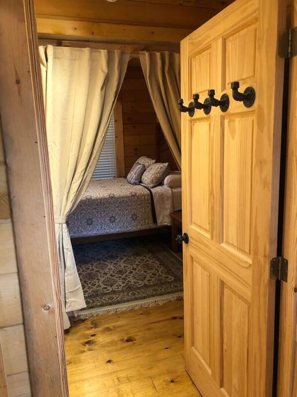 Une chambre dans une cabane en bois, avec un lit, des rideaux et une porte.
