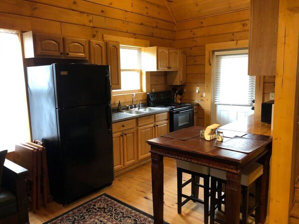 A wooden cabin kitchen with a black refrigerator, wooden cabinets, a stove, and a dining table.