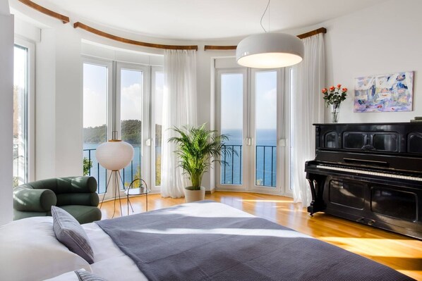 Ein Schlafzimmer mit Bett, Klavier, Topfpflanze und Meerblick.