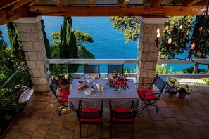 Un espace de restauration en plein air avec une table dressée pour deux personnes, entouré de piliers en pierre et offrant une vue sur une étendue d’eau.