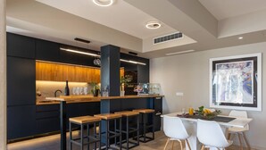 A modern kitchen with dark cabinetry, wooden bar stools, and a dining area with white chairs.
