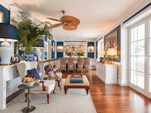A spacious living room with a dining area, large windows, and a ceiling fan.