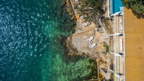 An aerial view of a coastal hotel with a clear blue sea, a sandy beach with sun loungers, and a building with a tiled facade. - Seafront Villa Dubrovnik Sea Diamant for 9 guests (Dubrovnik)