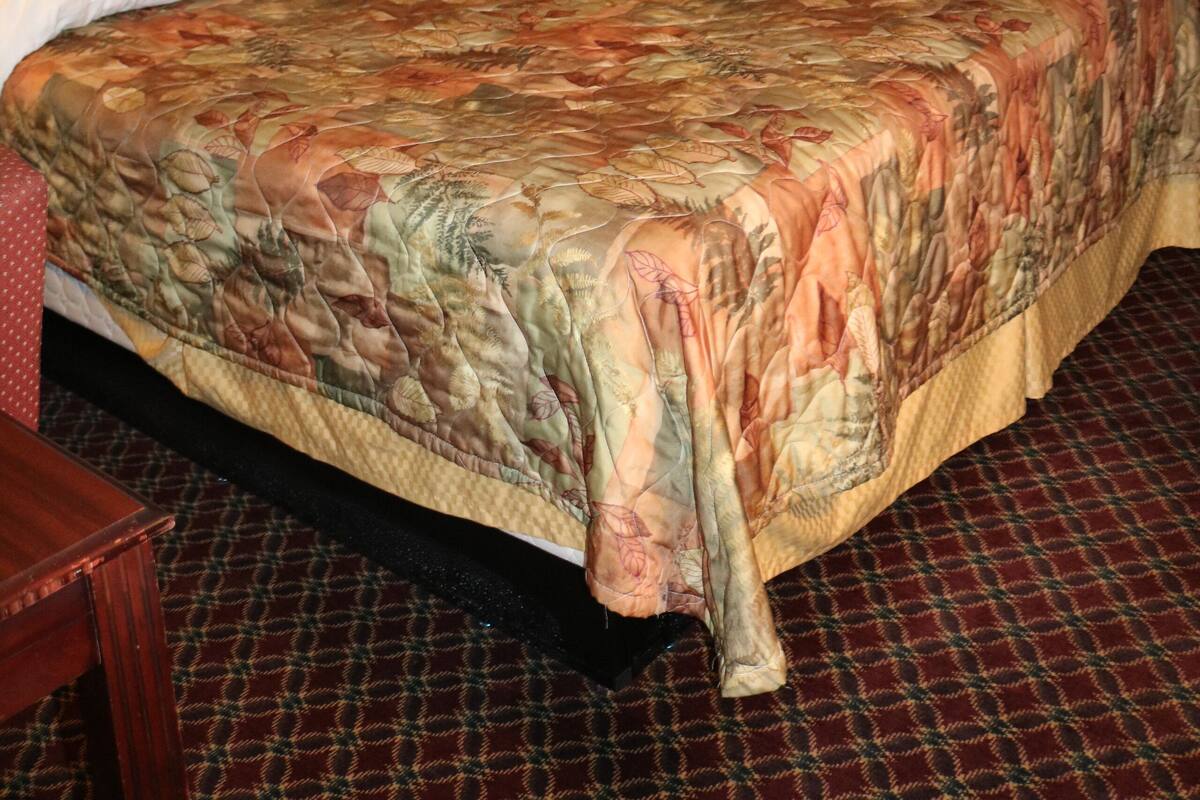 A hotel room with a large bed, a nightstand, a lamp, a chair, and a painting on the wall.