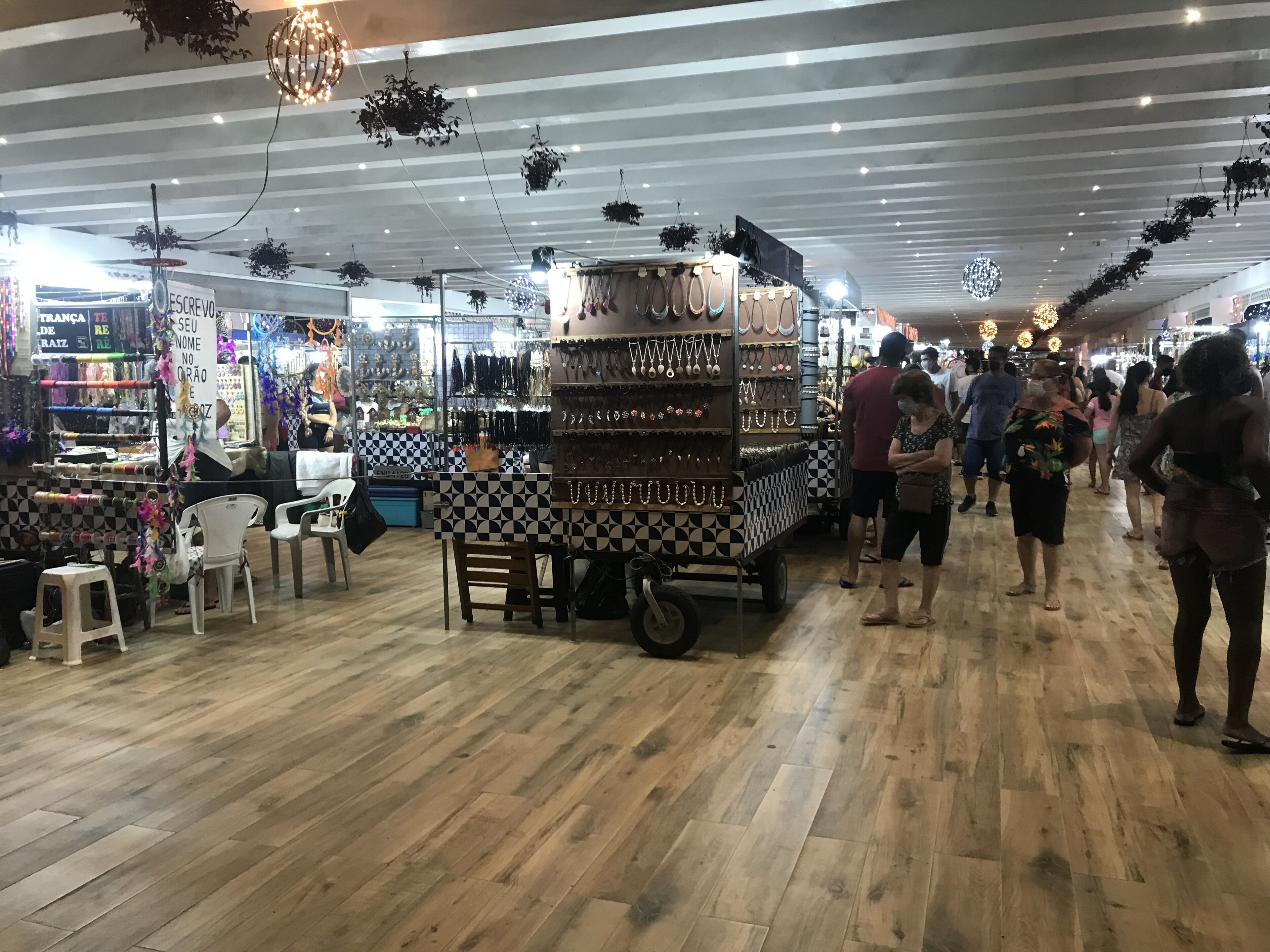 An indoor market with wooden flooring, stalls selling jewelry, and hanging plants.