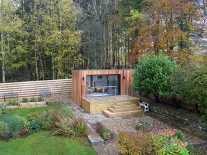 A wooden cabin with a glass door, surrounded by a garden with various plants and a wooden deck. - 2 bedroom accommodation in Ayr (Ayr)