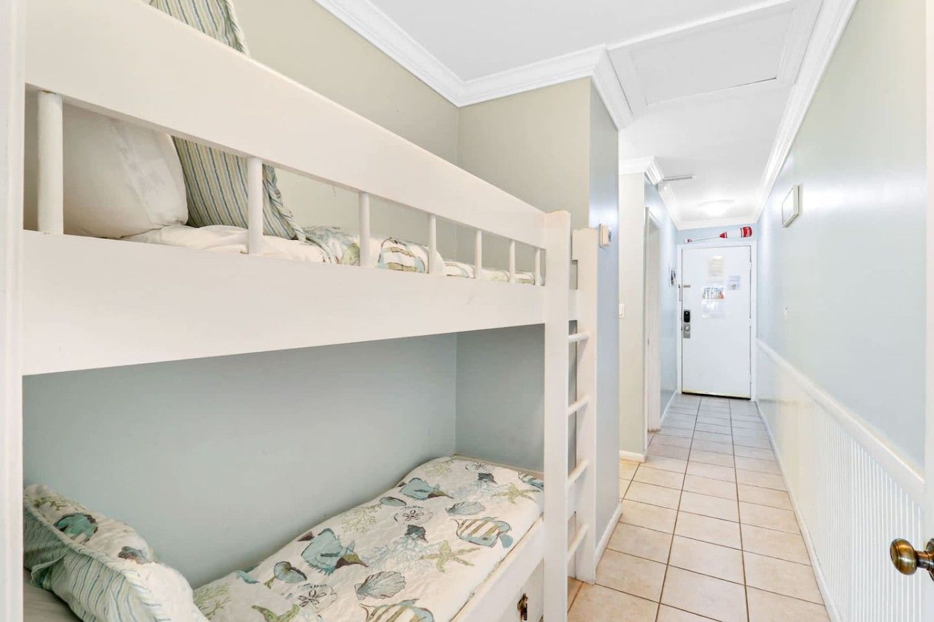 A hotel room with bunk beds, a hallway with a door, and a tiled floor.