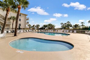 A swimming pool with lounge chairs and palm trees, surrounded by a building with balconies.
