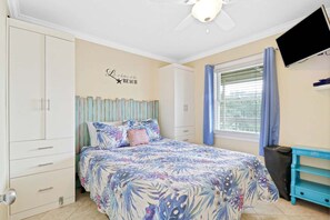 A bedroom with a bed, wardrobe, ceiling fan, window with curtains, and a TV on the wall.