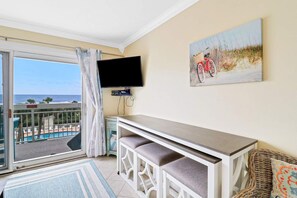A balcony with a view of the ocean, a television mounted on the wall, and a painting of a bicycle.