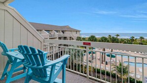 Un balcone con sedie blu, zona piscina e vista sulla spiaggia.