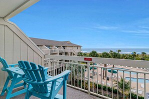 A balcony with blue chairs, a pool area, and a view of the beach.