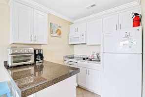 A kitchen with white cabinets, a double oven, a coffee maker, a microwave, a sink, and a refrigerator with a fire extinguisher.
