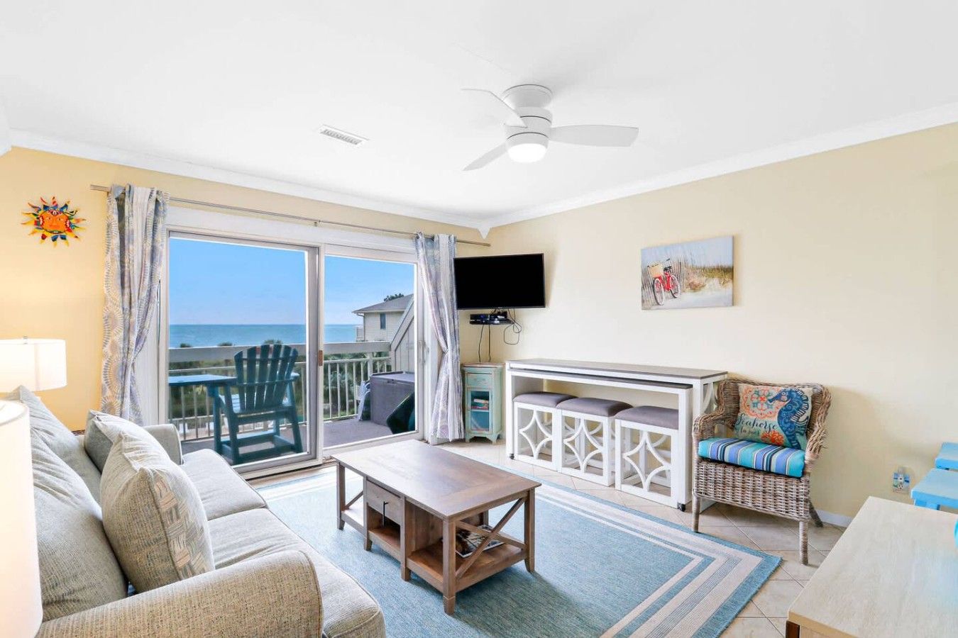 Een woonkamer met een bank, een salontafel, een televisie en een balkon met uitzicht op zee.